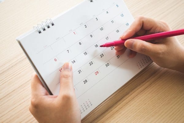 hand-with-pen-writing-calendar-page-closeup-scaled-e1660894894615 Hands marking a date on desk calendar